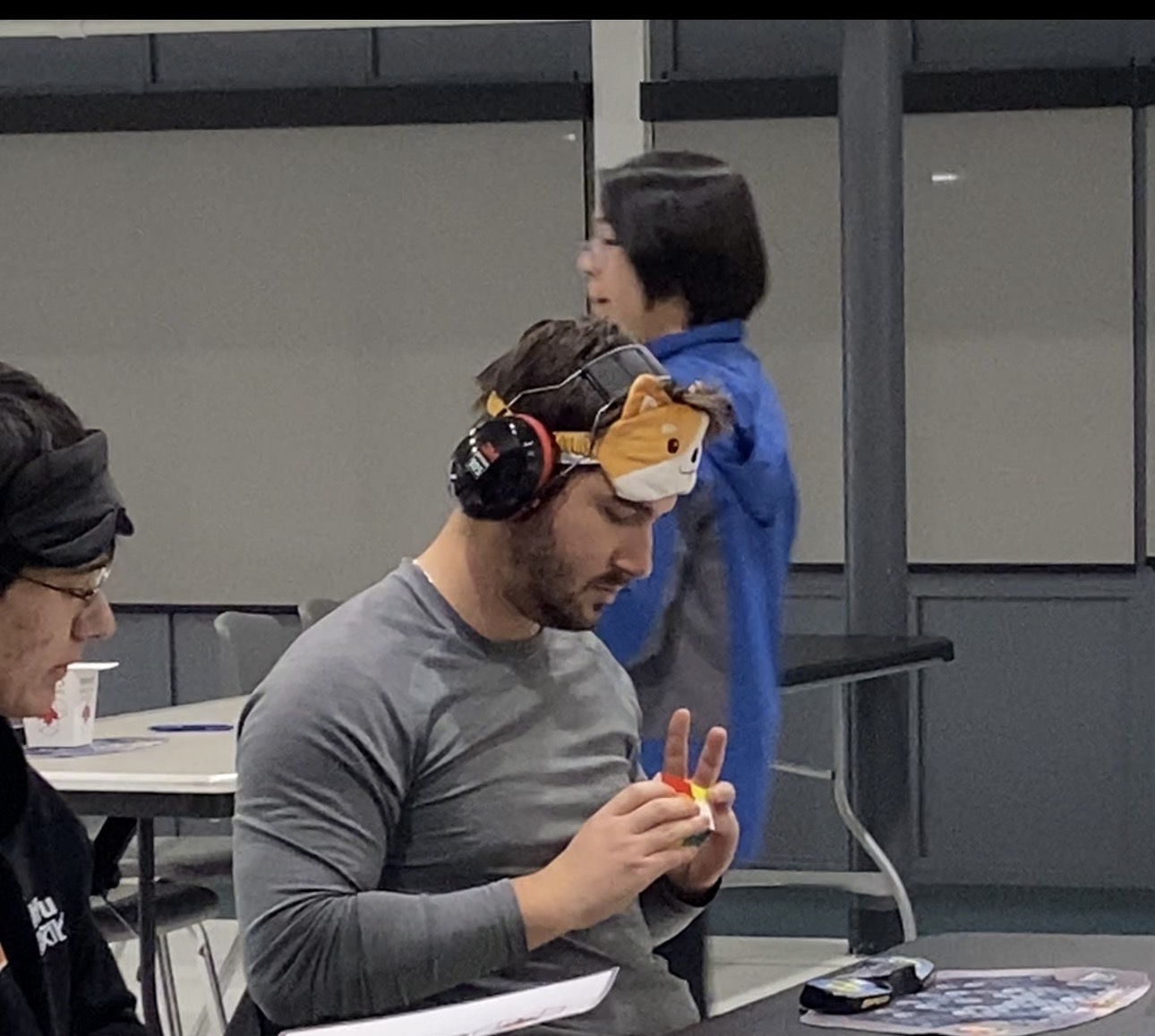 William Kitching at a cubing competition, holding a cube and wearing a blindfold and headphones